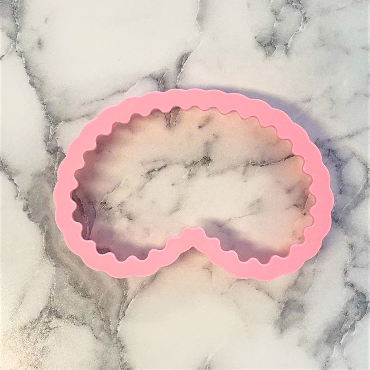 Pink silicone face mask cookie cutter mold with scalloped edges for crafting skincare product designs