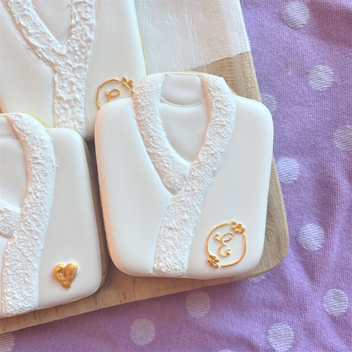 White frosted robe-shaped cookie with lace detailing and gold icing accents from spa cookie cutter bundle