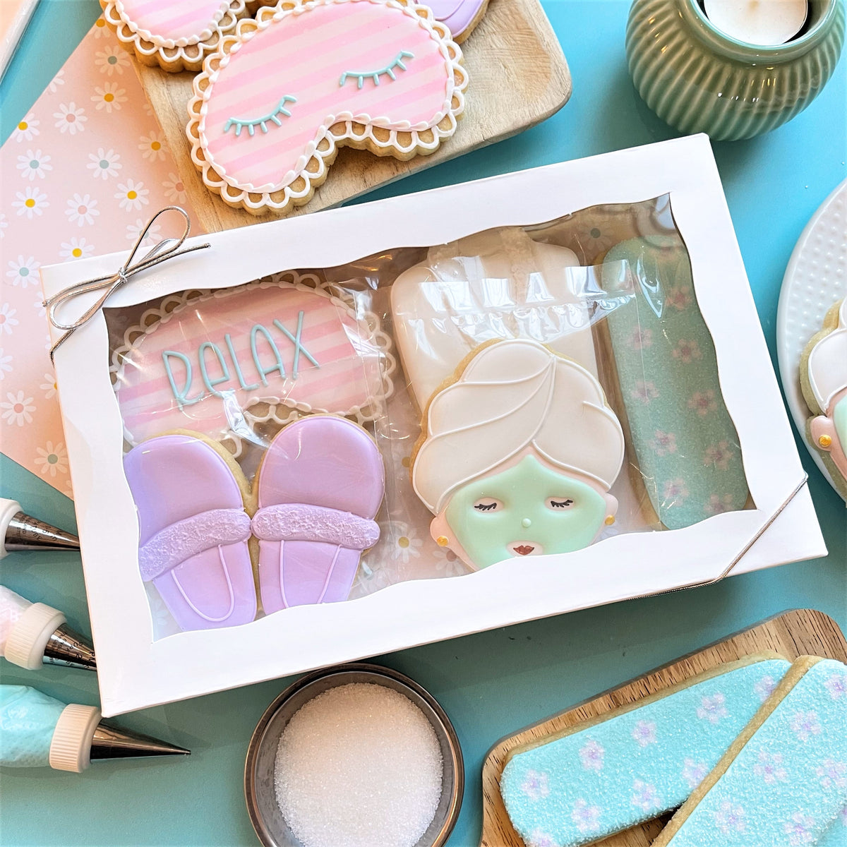 A white rectangular box with a clear window containing decorated sugar cookies shaped like sleep masks slippers and facial treatments