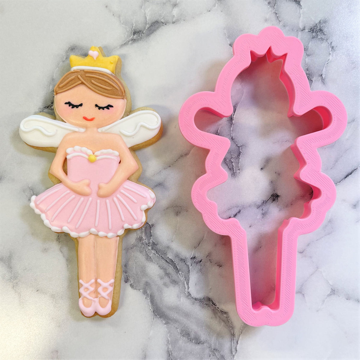 Pink plastic sugar plum fairy cookie cutter next to decorated sugar cookie shaped like ballet dancer figure