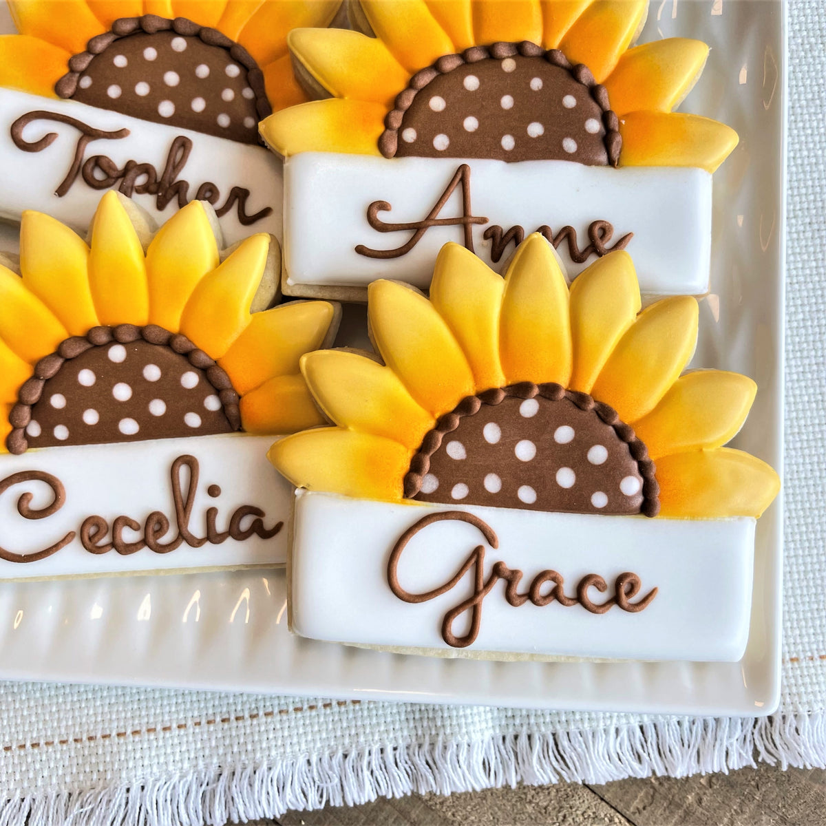 Sunflower plaque cookie cutter shaped cookies with yellow petals brown centers and white bases with chocolate lettering