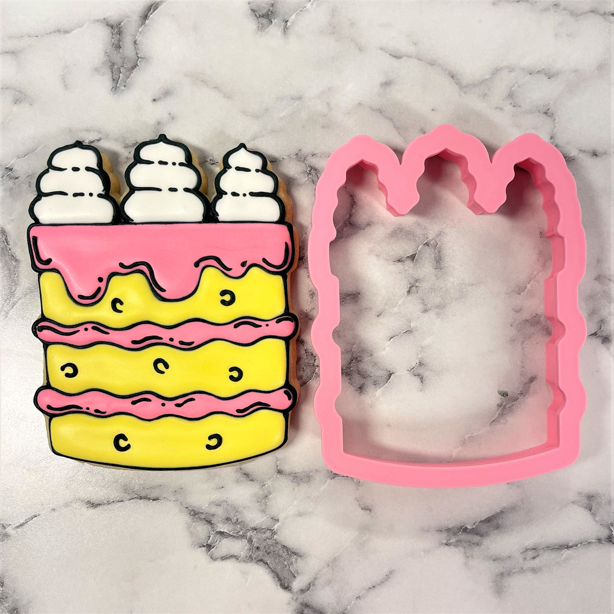 Tall cake cookie cutter made of pink silicone with whimsical multi-layered yellow cake and pink frosting details