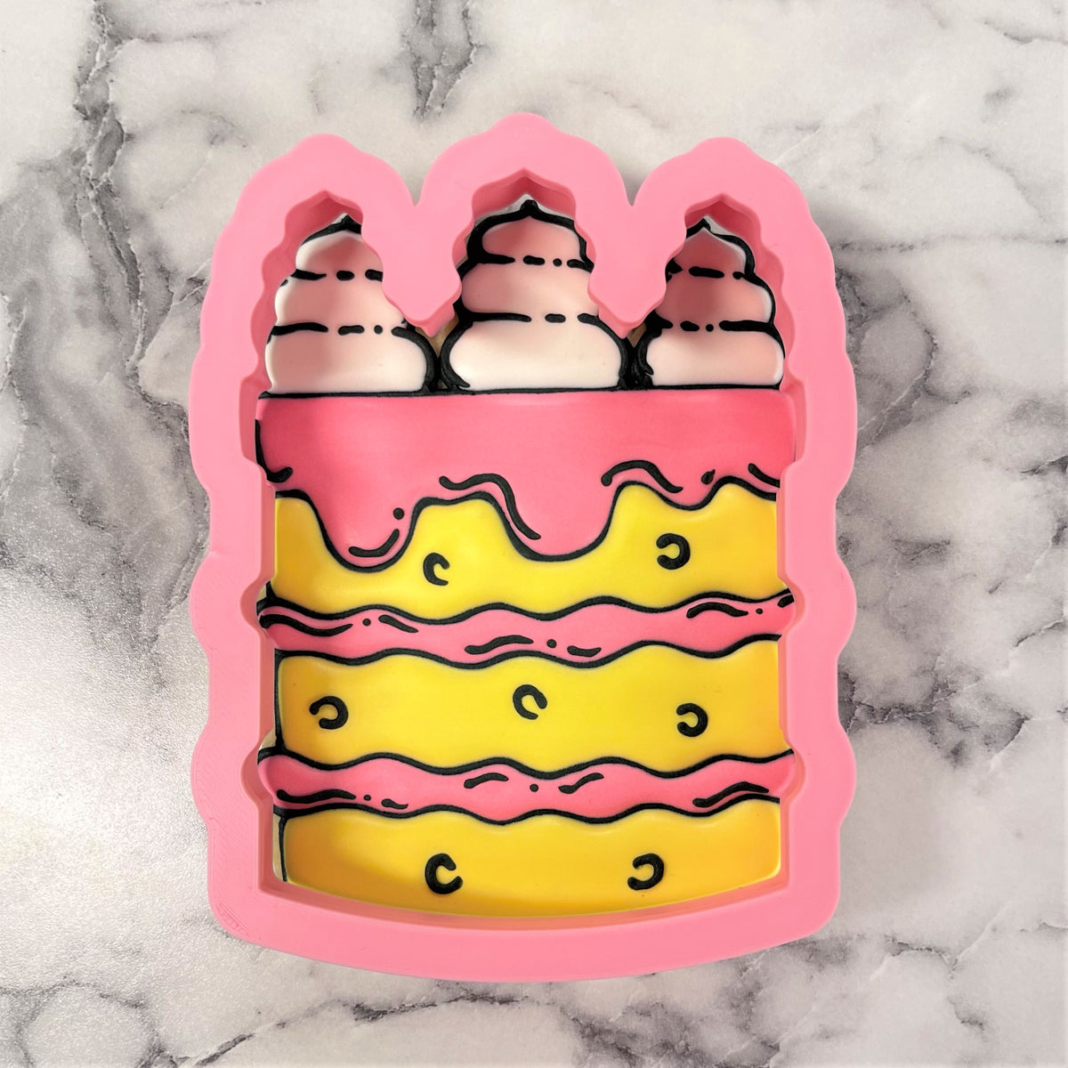 Pink silicone tall cake cookie cutter with yellow layers pink frosting and three white whipped cream swirls on top