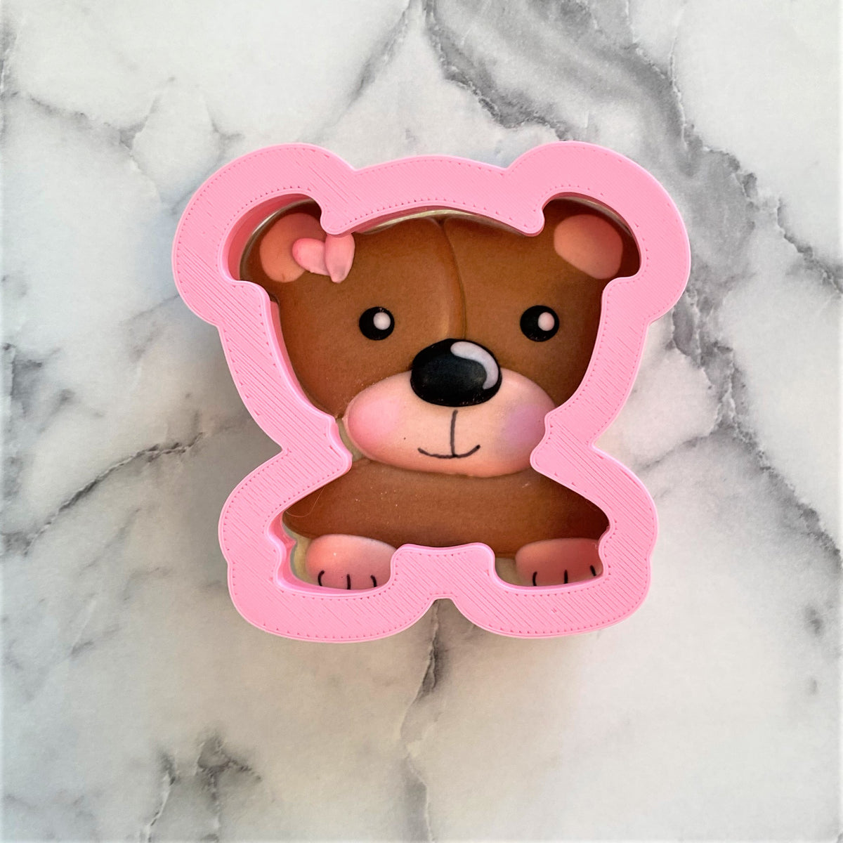 Pink plastic teddy bear bust cookie cutter with brown fondant bear featuring black eyes and nose inside