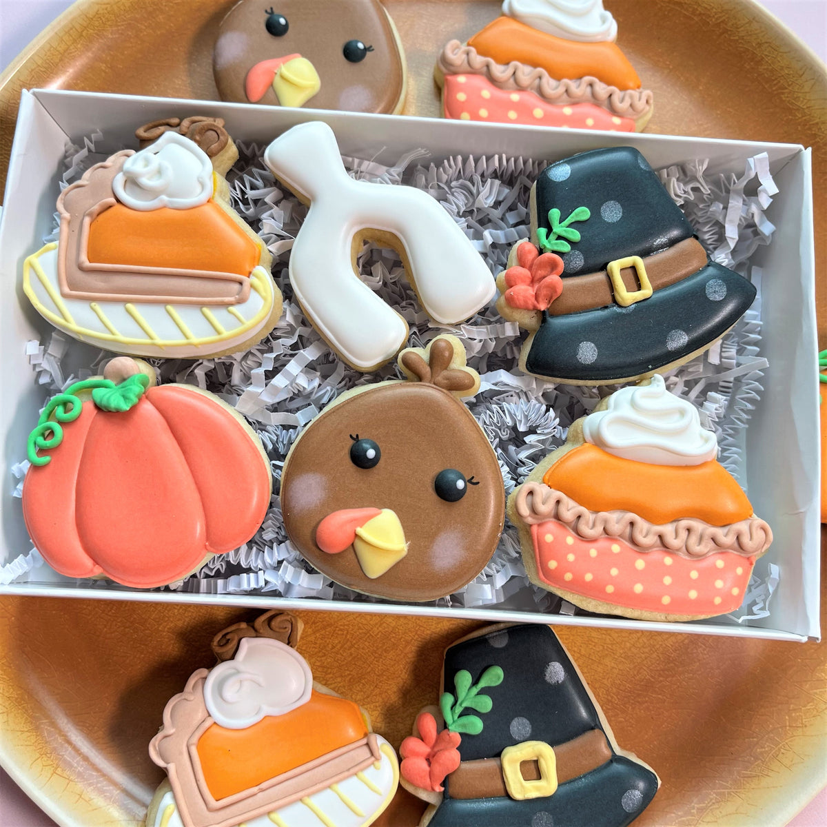 A box of thanksgiving-themed sugar cookies with pumpkins pie slices and pilgrim hats decorated with vibrant icing