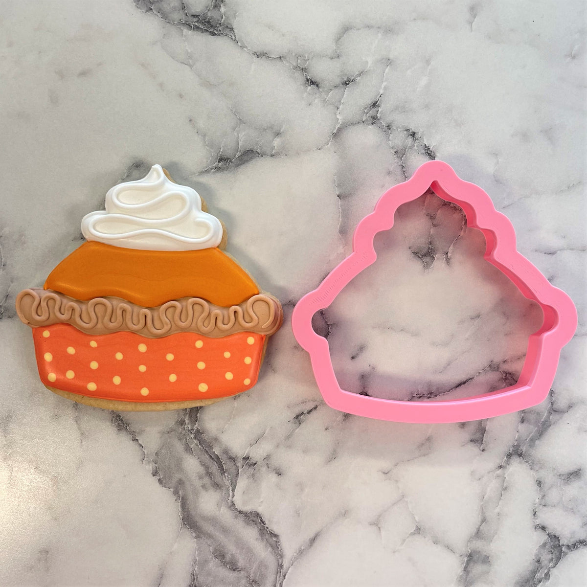 A pink silicone thanksgiving pie cookie cutter next to a decorated orange pumpkin pie-shaped sugar cookie