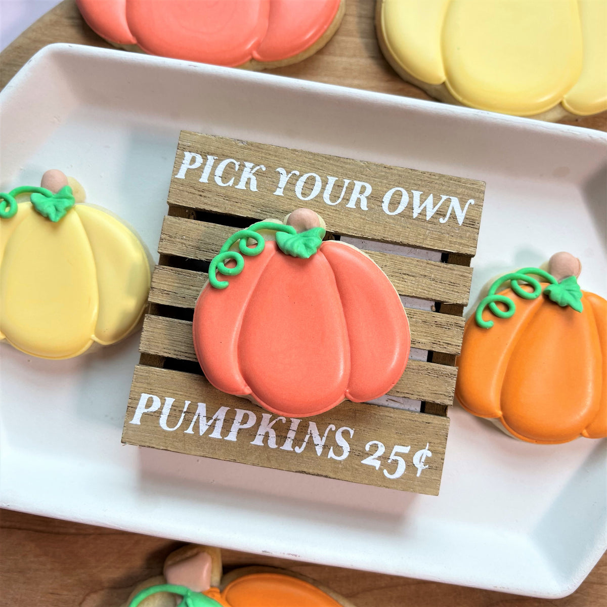 Mini thanksgiving pumpkin cookie cutter used to make a glossy orange pumpkin shaped cookie with green icing vines and a brown stem