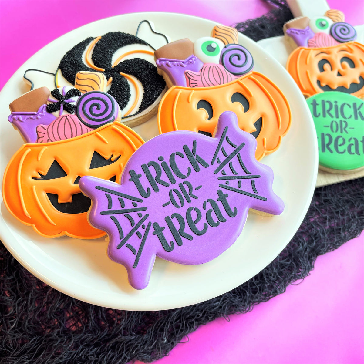 Purple spiderweb-shaped cookie with trick-or-treat text and black icing made using candy jack-o-lantern flour box club cutter