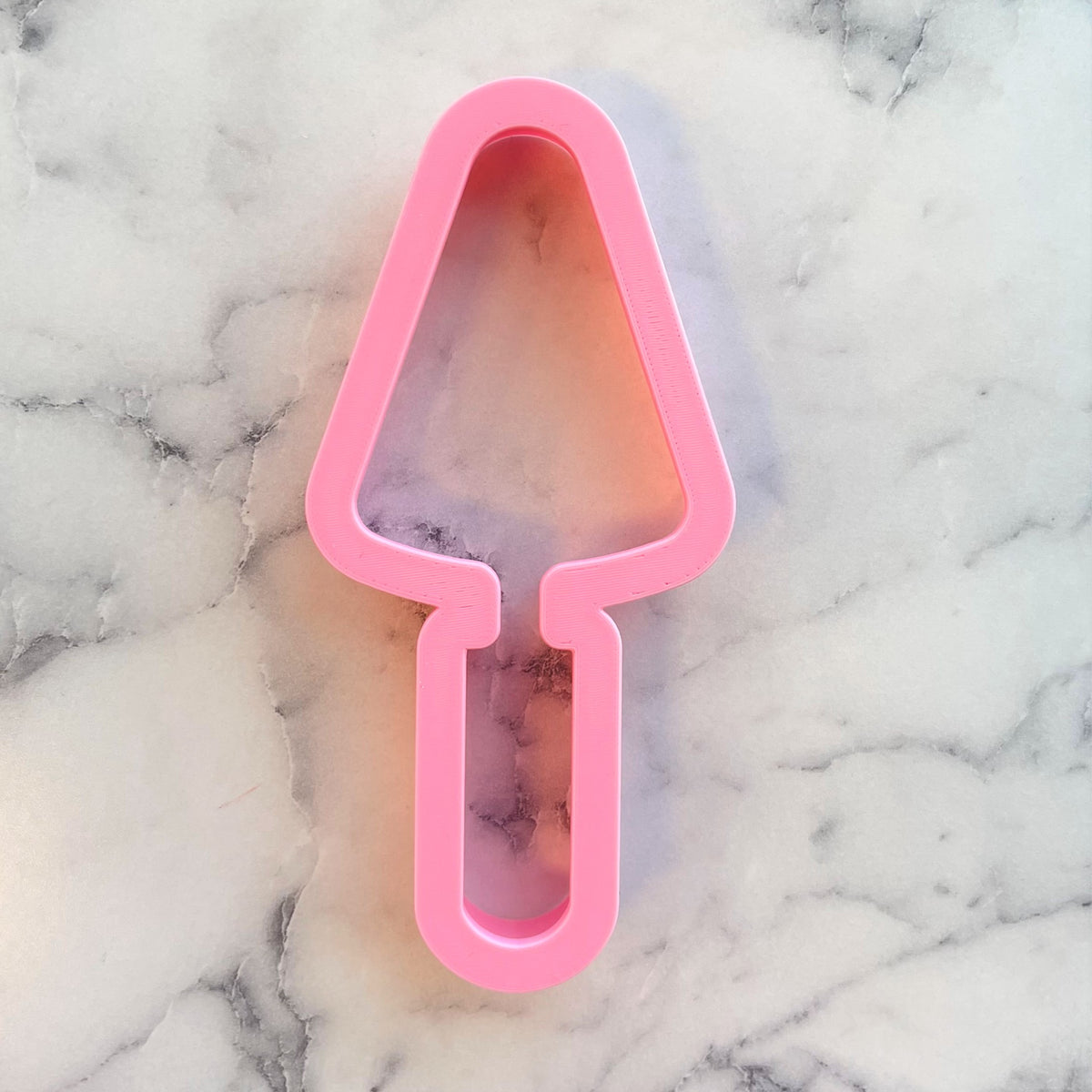 Pink plastic trowel cookie cutter shaped like a cake server for baking and decorating cookies