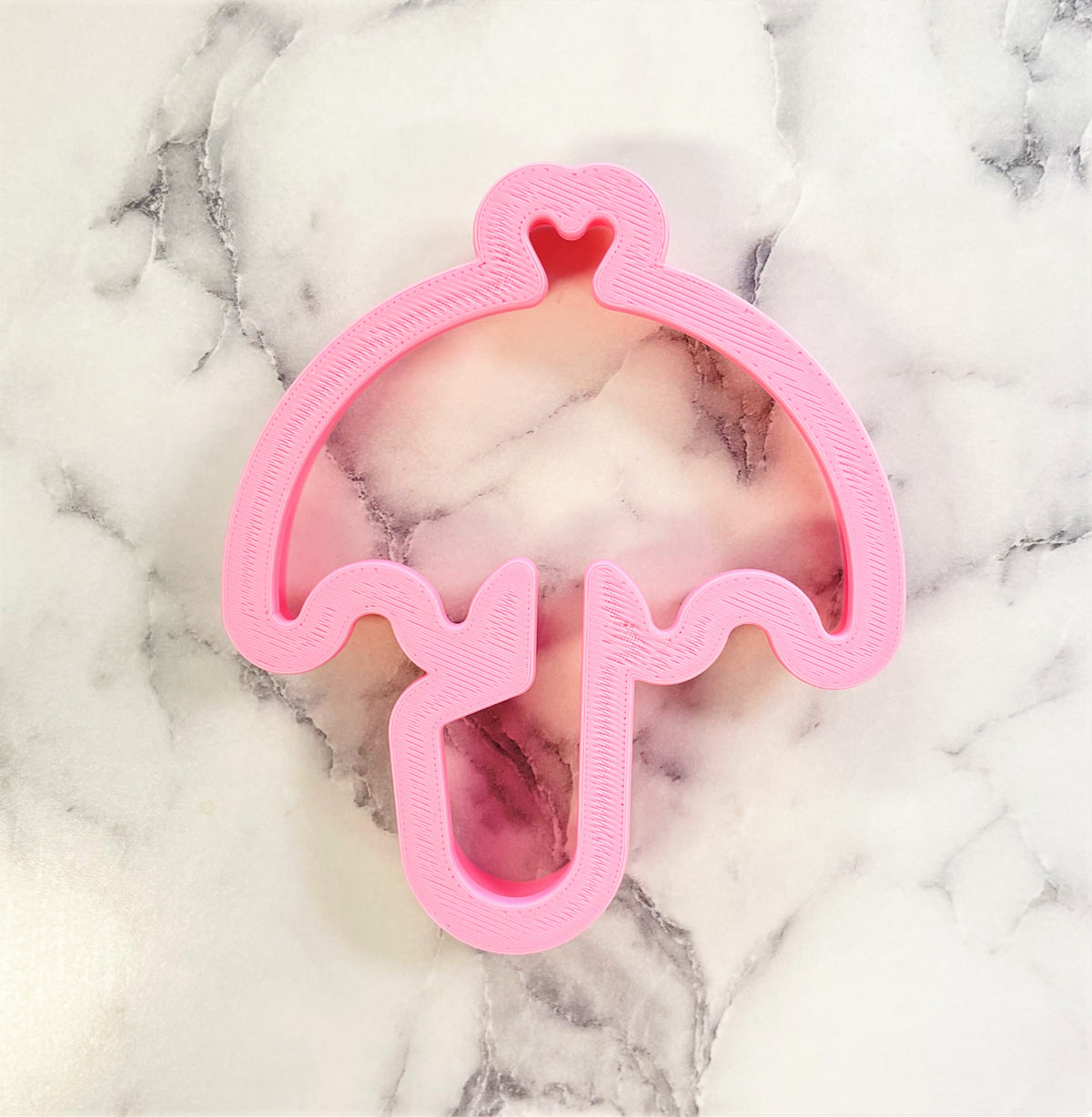 Pink plastic umbrella cookie cutter with a heart detail at the top for baking and decorating treats