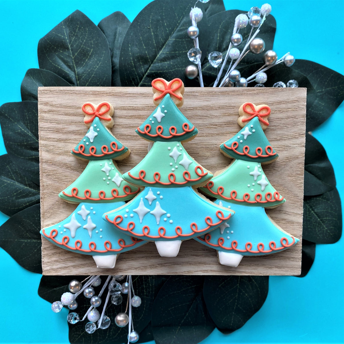 Three turquoise and light blue vintage christmas tree cookies decorated with orange bows and white star patterns