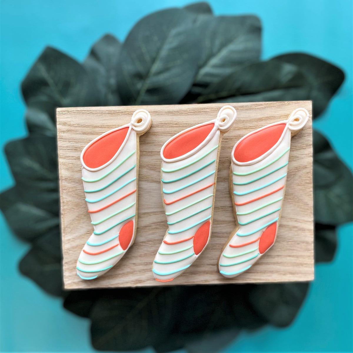 Three decorated sugar cookies shaped like christmas stockings with white, orange, and light blue icing from vintage christmas cookie cutter set