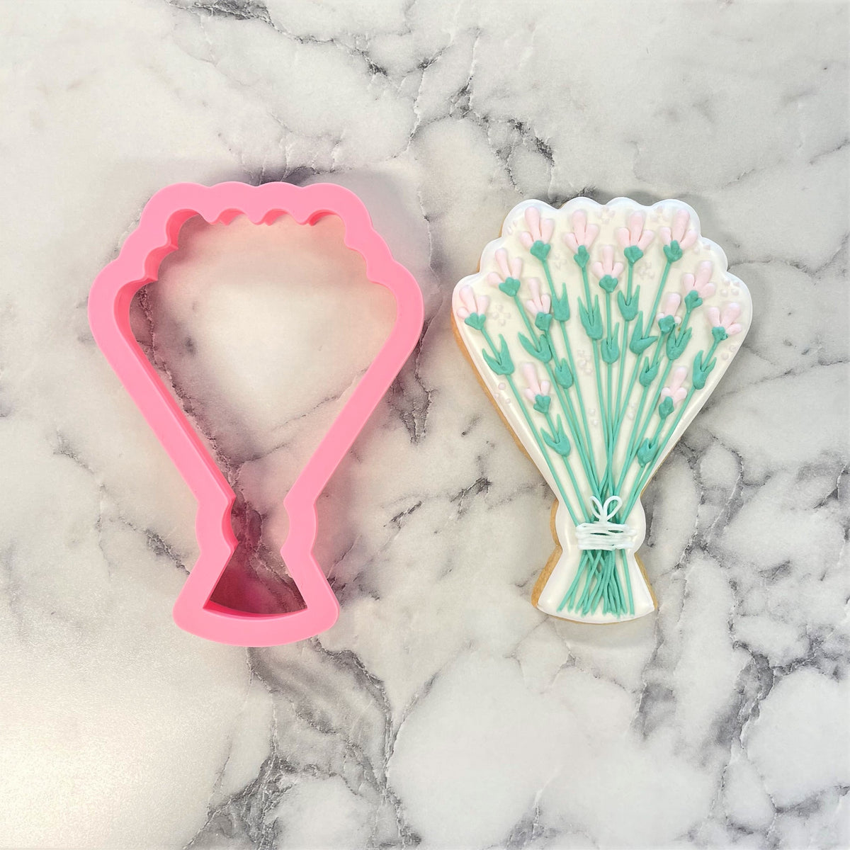 Pink silicone wedding bouquet cookie cutter next to decorated sugar cookie shaped like lavender bouquet design