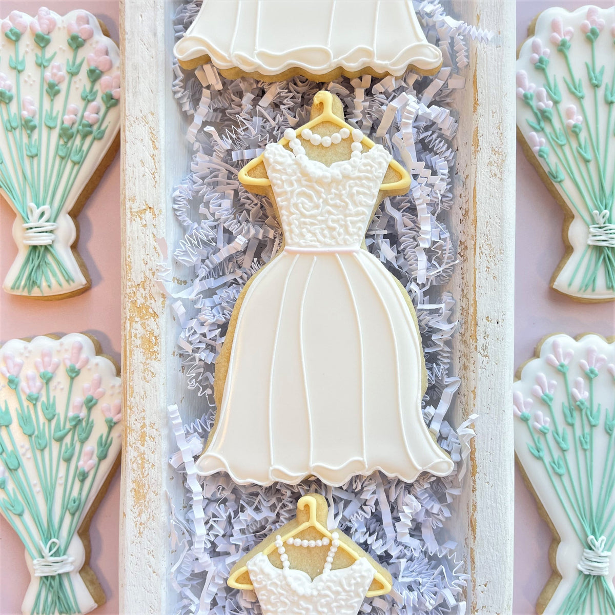 A delicate white lace wedding dress cookie with intricate piped icing on a yellow hanger for wedding bouquet cutter