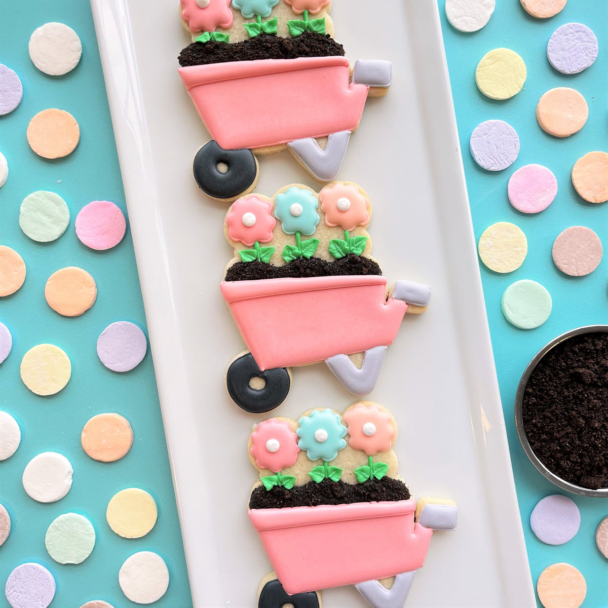 Pink sugar cookie wheelbarrows with colorful flower decorations and black wheels from gardening mothers day cookie cutter set