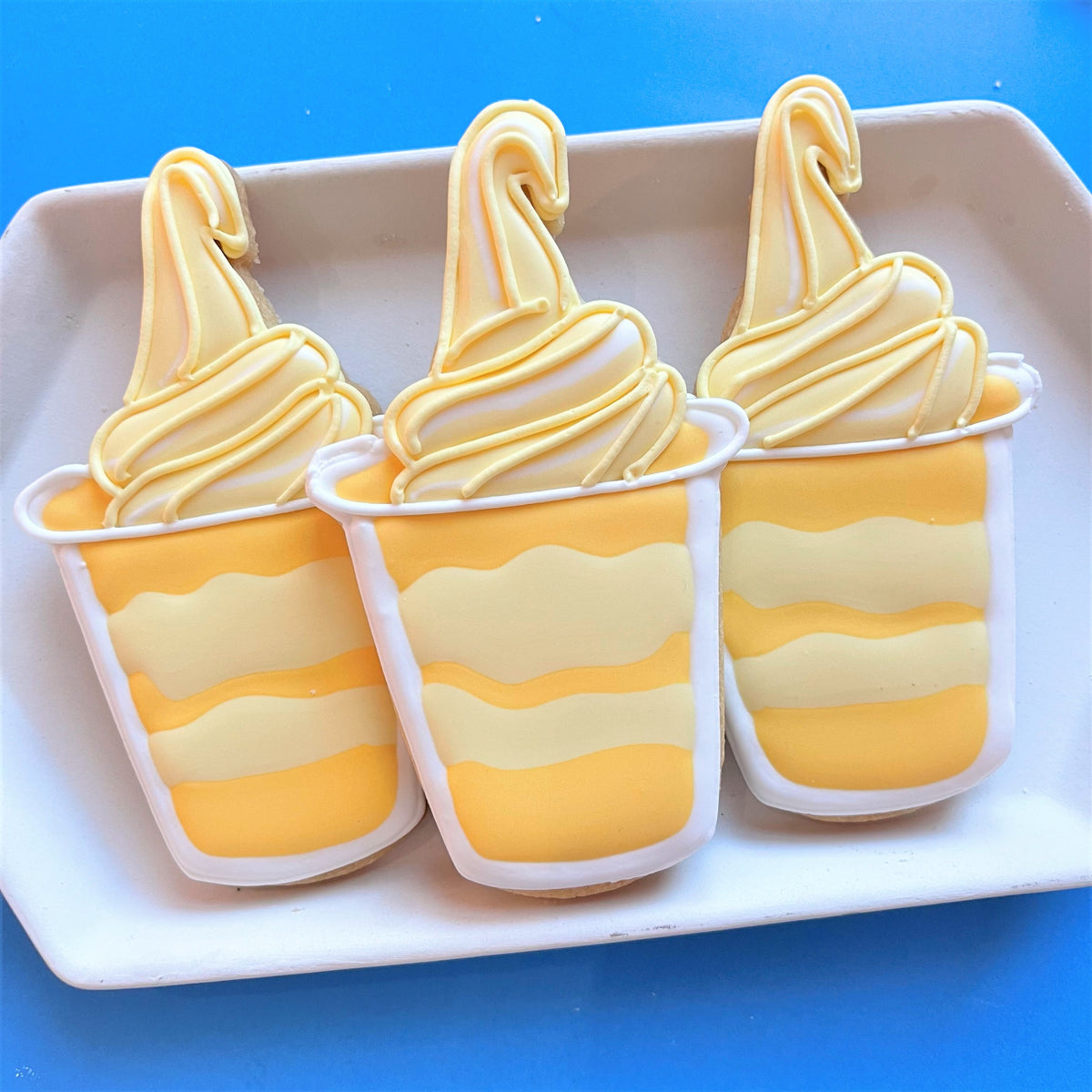 Three yellow and white soft-serve ice cream cookie cups with swirled frosting from mouse snacks online cookie decorating class recording