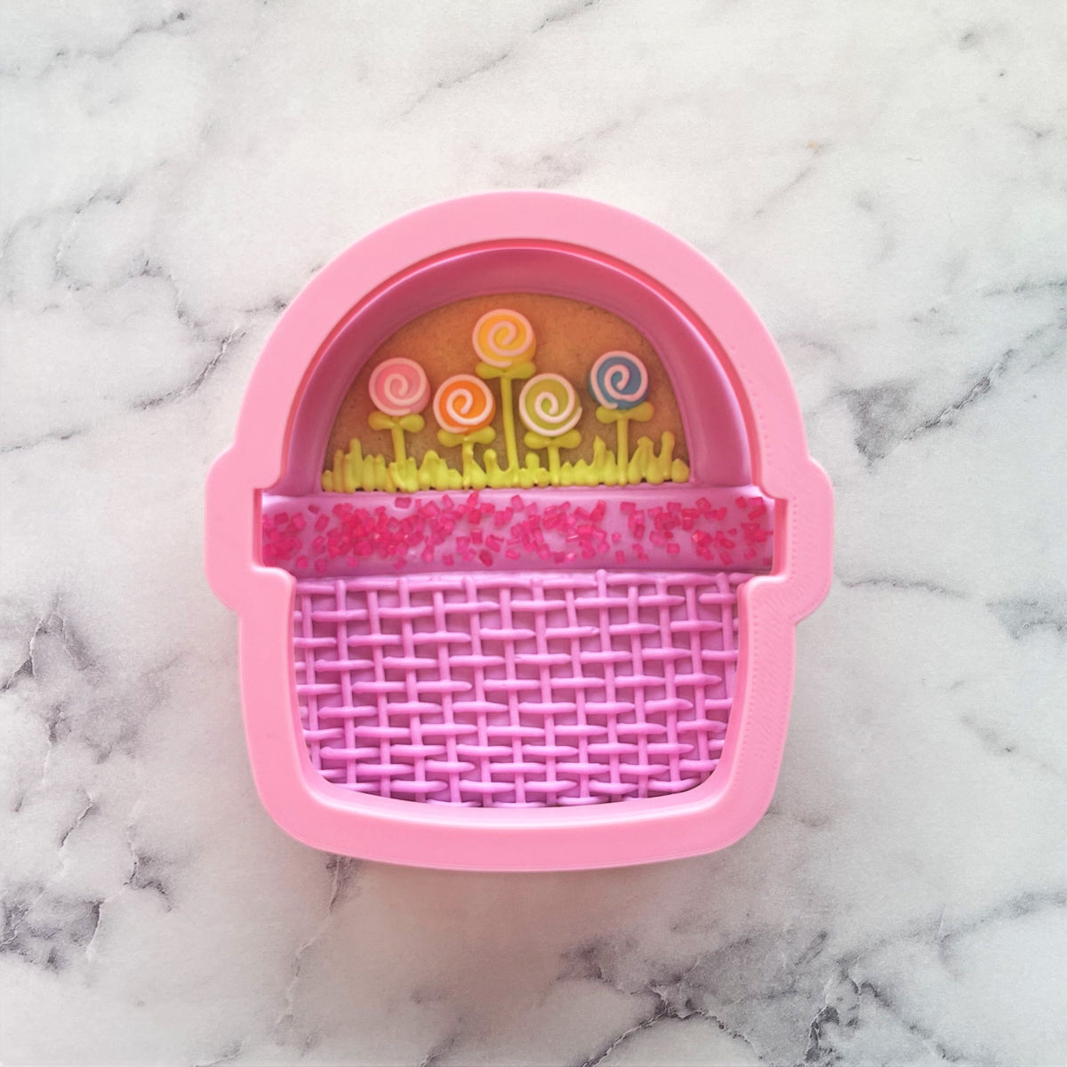 Wide basket cookie cutter in pink silicone with woven texture and colorful candy-themed interior design