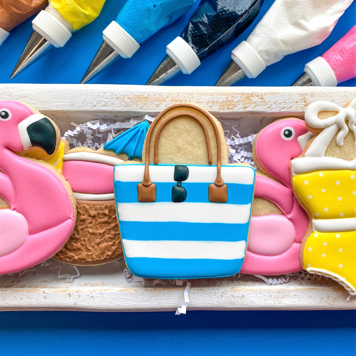Blue and white striped sugar cookie shaped like a beach tote bag with brown handles and black sunglasses from pool party cookie cutter set