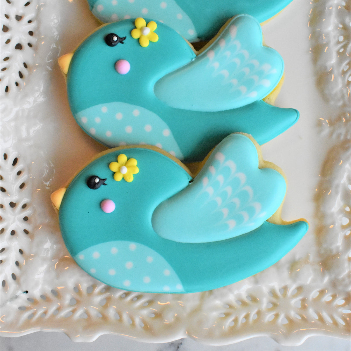 Cute turquoise bird-shaped cookies decorated with yellow flowers and white polka dots from springtime online decorating class recording