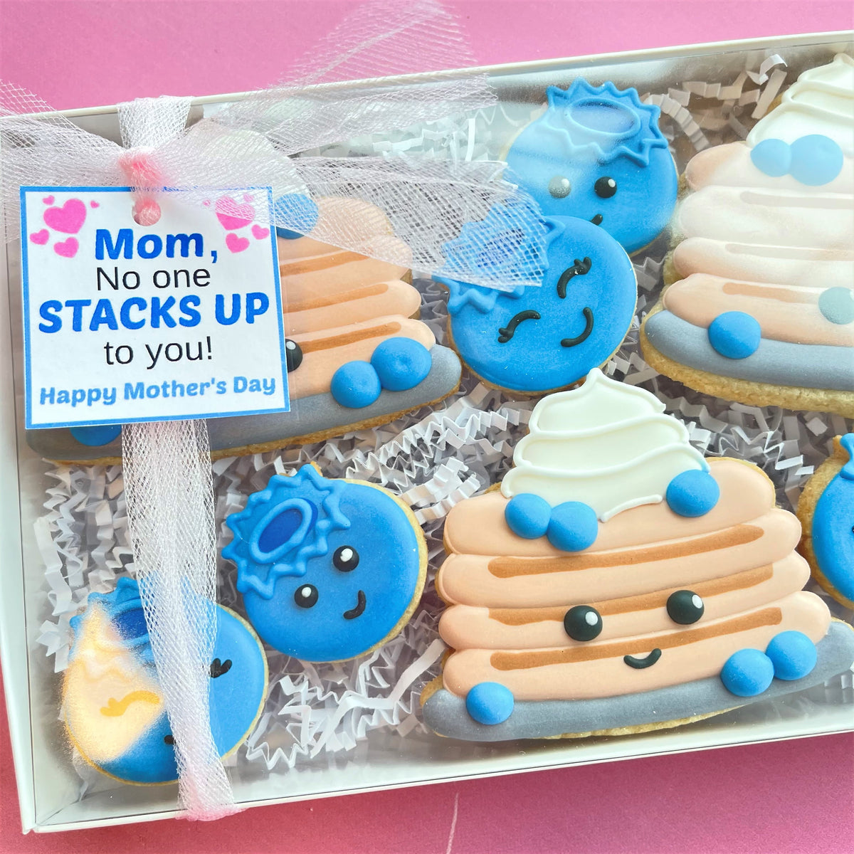 A charmingly decorated box of blueberry and pancake themed sugar cookies with cheerful cartoon faces made from icing