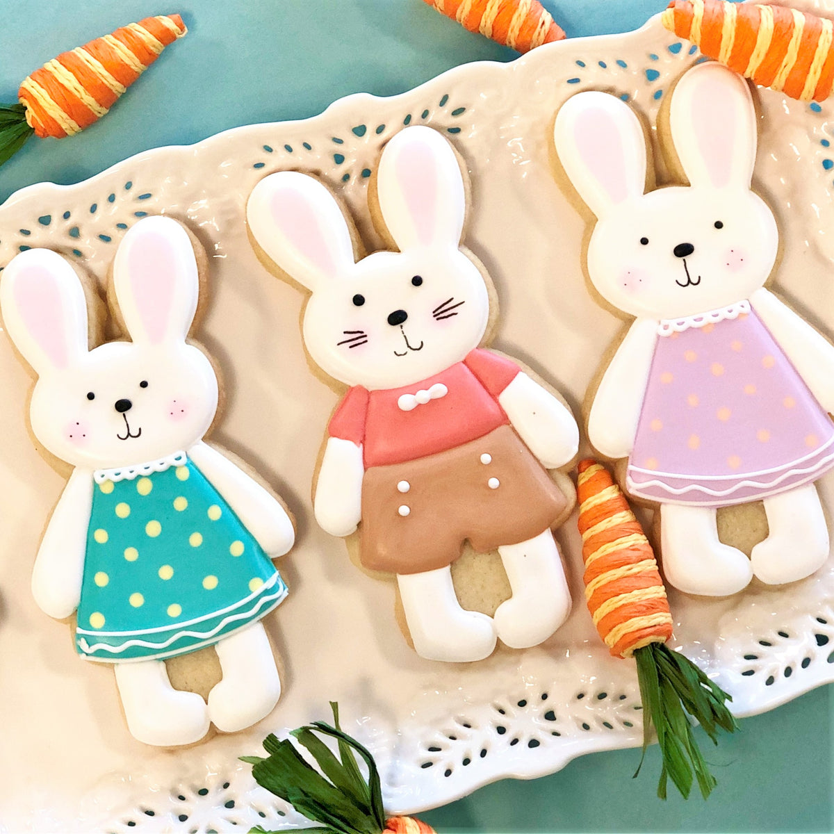 Three intricately decorated standing bunny sugar cookies with colorful icing dresses and carrot accessories