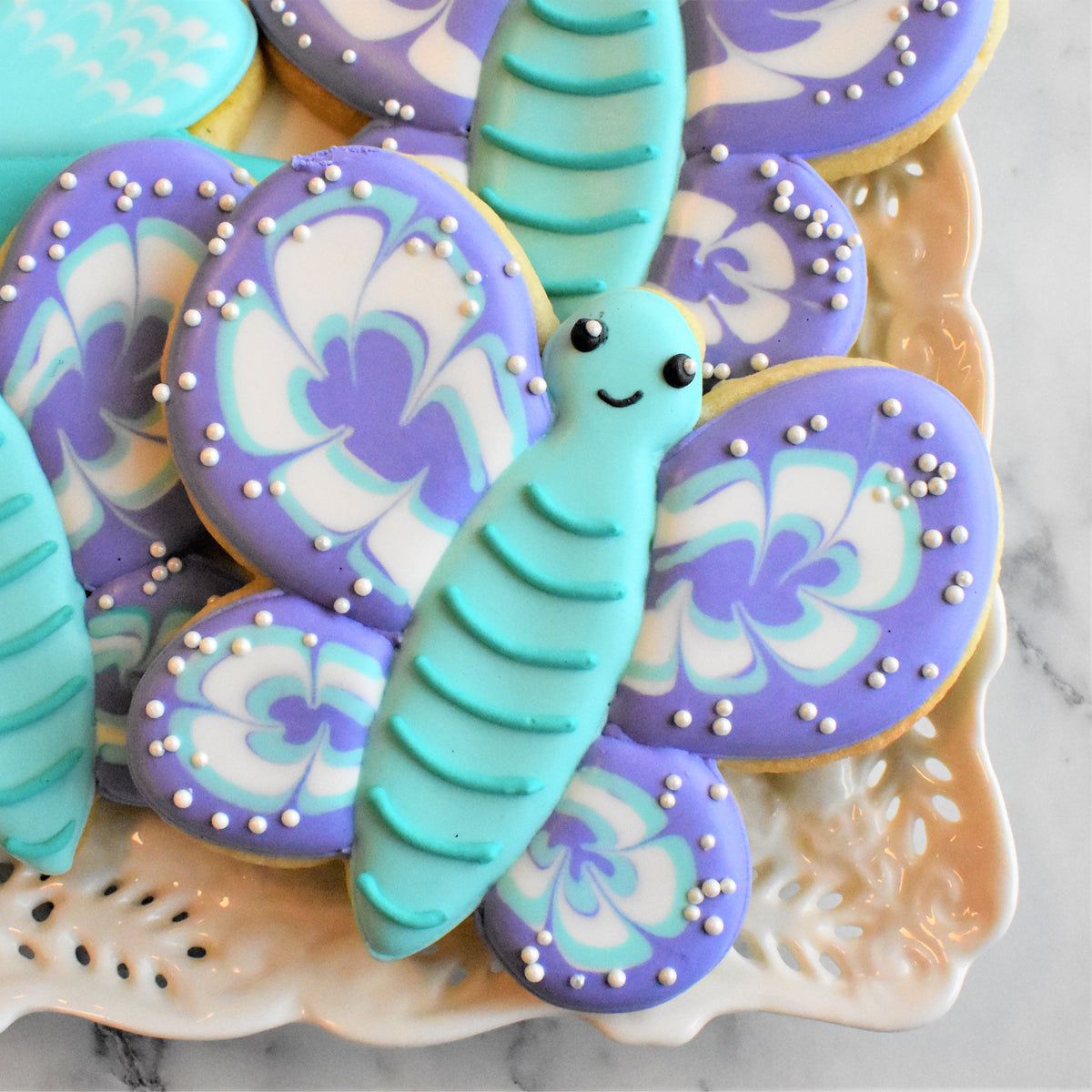 A turquoise butterfly-shaped cookie decorated with white sugar pearls from the springtime online decorating class recording