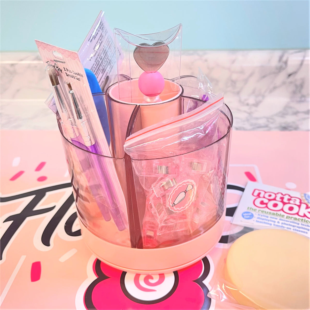 Pink translucent cookie decorating tool spinning caddy with heart-shaped top and multiple compartments holding craft supplies