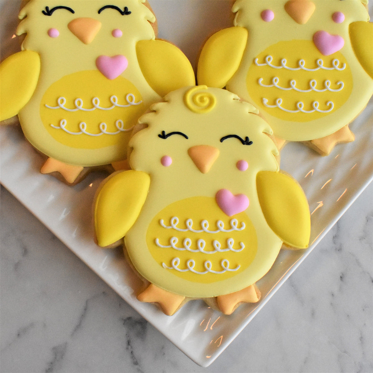 Yellow chick-shaped cookies with pink hearts and white icing details from springtime online decorating class recording