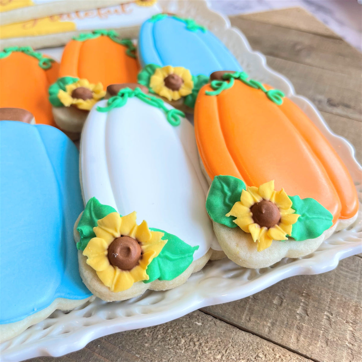 Orange and white pumpkin-shaped sugar cookies decorated with yellow sunflower icing made using pumpkin tall with sunflower cookie cutter