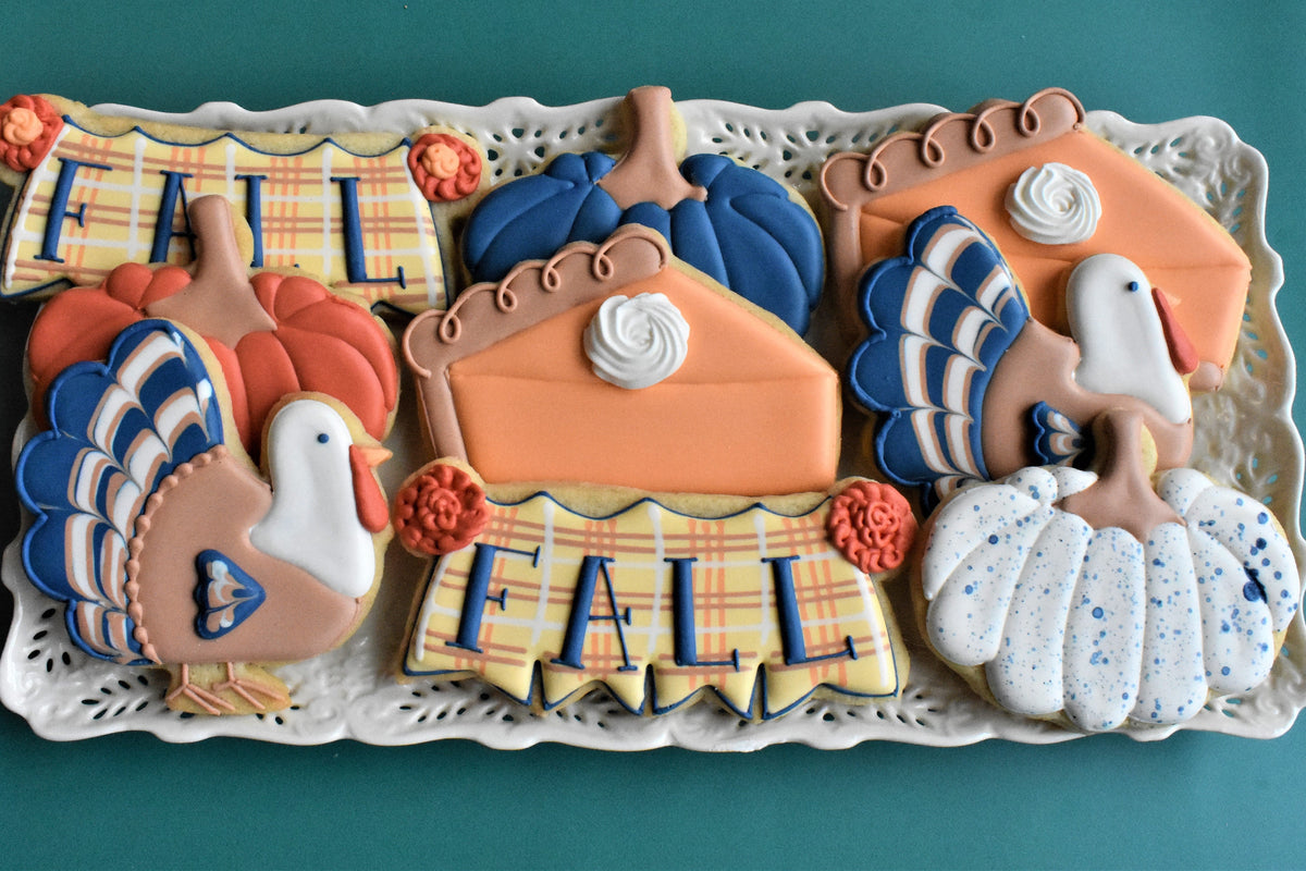 Ornate fall-themed sugar cookies shaped like turkeys pumpkins and pie slices with detailed orange blue white and yellow icing for thanksgiving decorating class recording