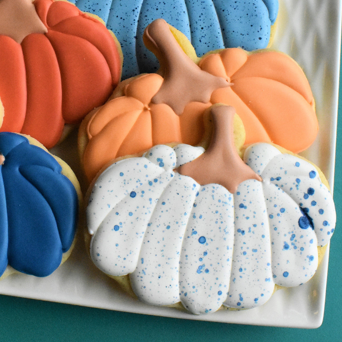 A white pumpkin-shaped cookie with blue speckles and tan stem frosted in smooth icing from fall thanksgiving decorating class recording