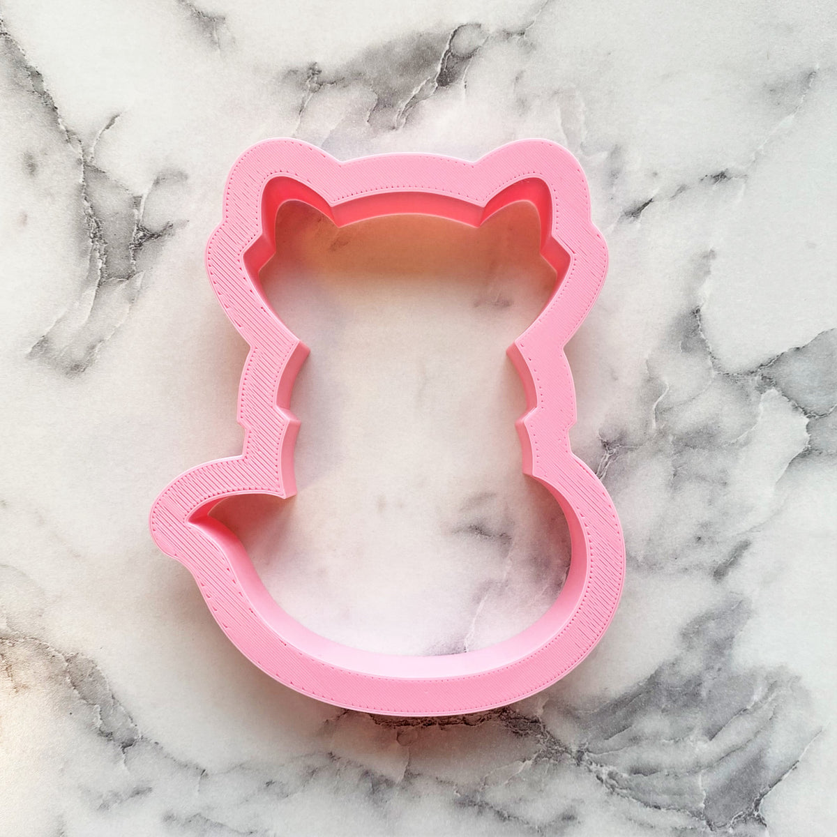 Pink plastic cat-shaped cookie cutter with rounded ears and tail for woodland fox baking projects