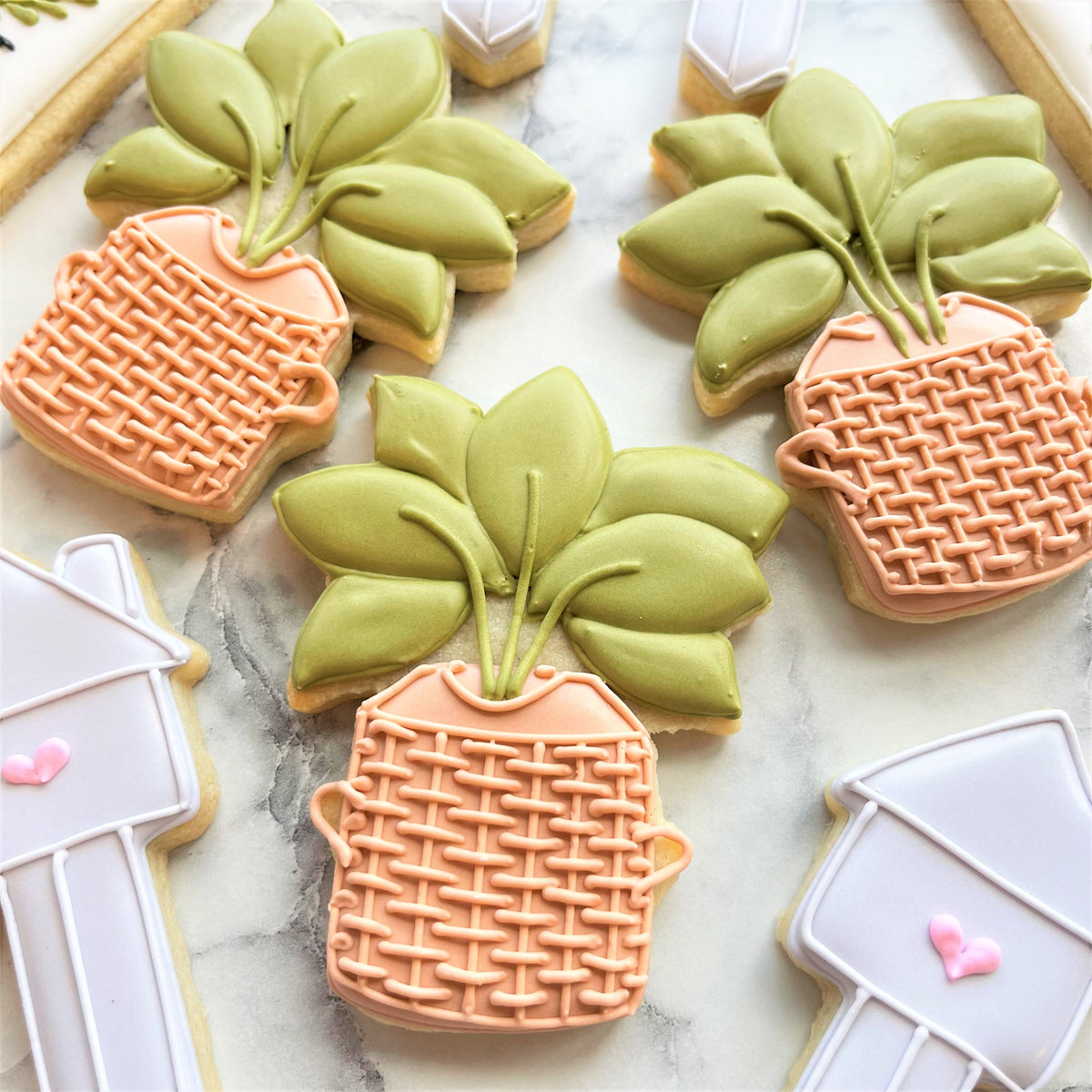 Pastel peach sugar cookies shaped like woven planters with green leafy tops from housewarming cookie cutter set