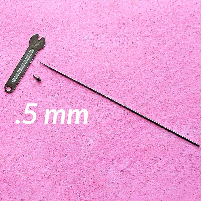 A slender metallic 0.5 mm airbrush gun nozzle replacement needle with wrench and screw on pink surface