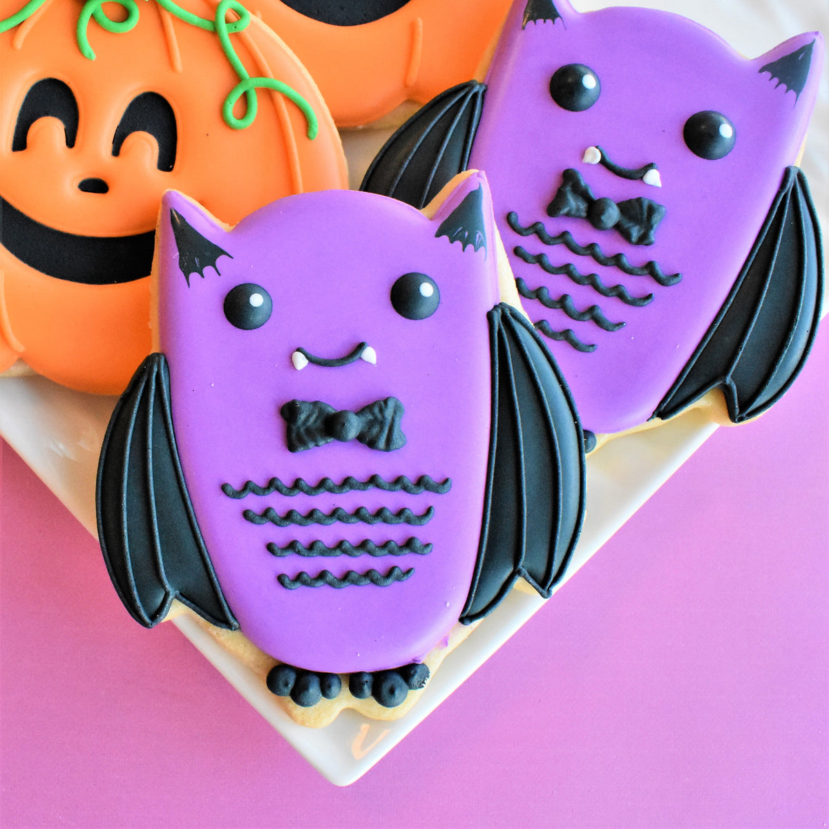 Purple bat-shaped cookies with black icing wings bow tie and eyes from spooktacular online decorating class recording