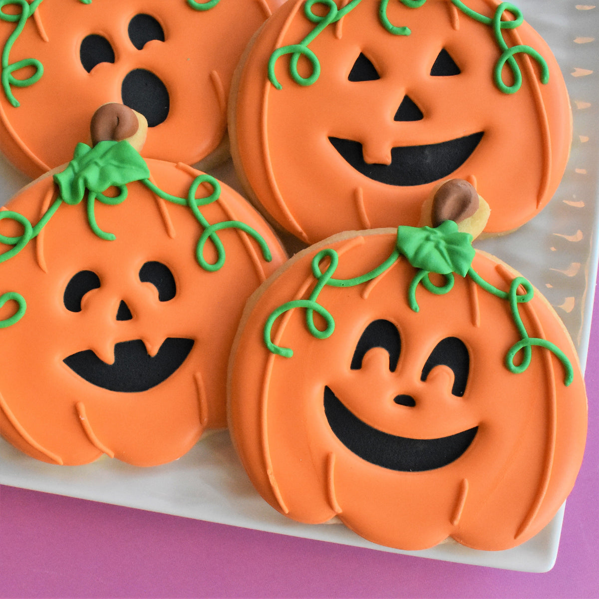Orange pumpkin-shaped cookies with black icing faces and green vines from spooktacular online decorating class recording