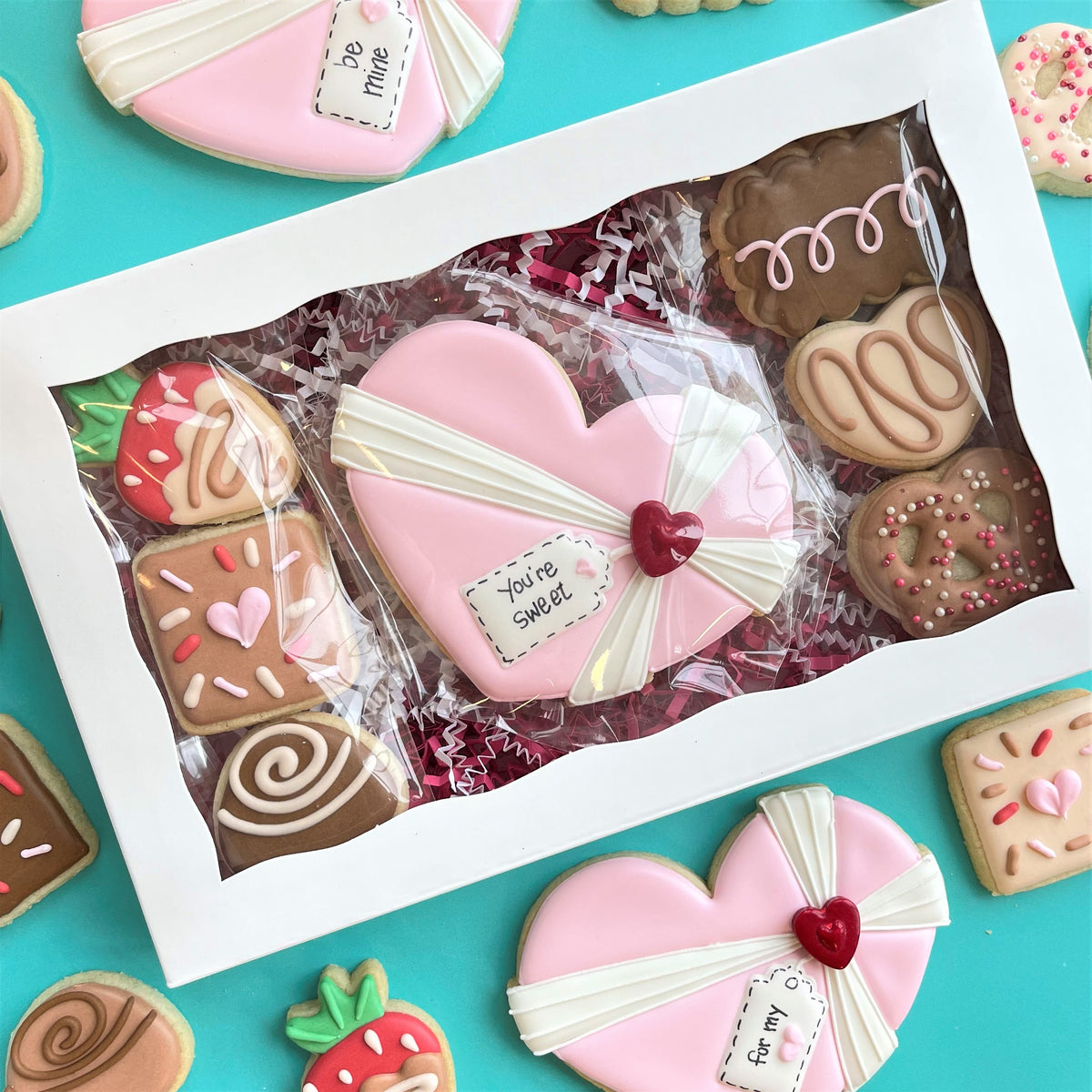 A pink heart-shaped cookie with white icing ribbon and red heart accent made using chocolate heart box cookie cutter set