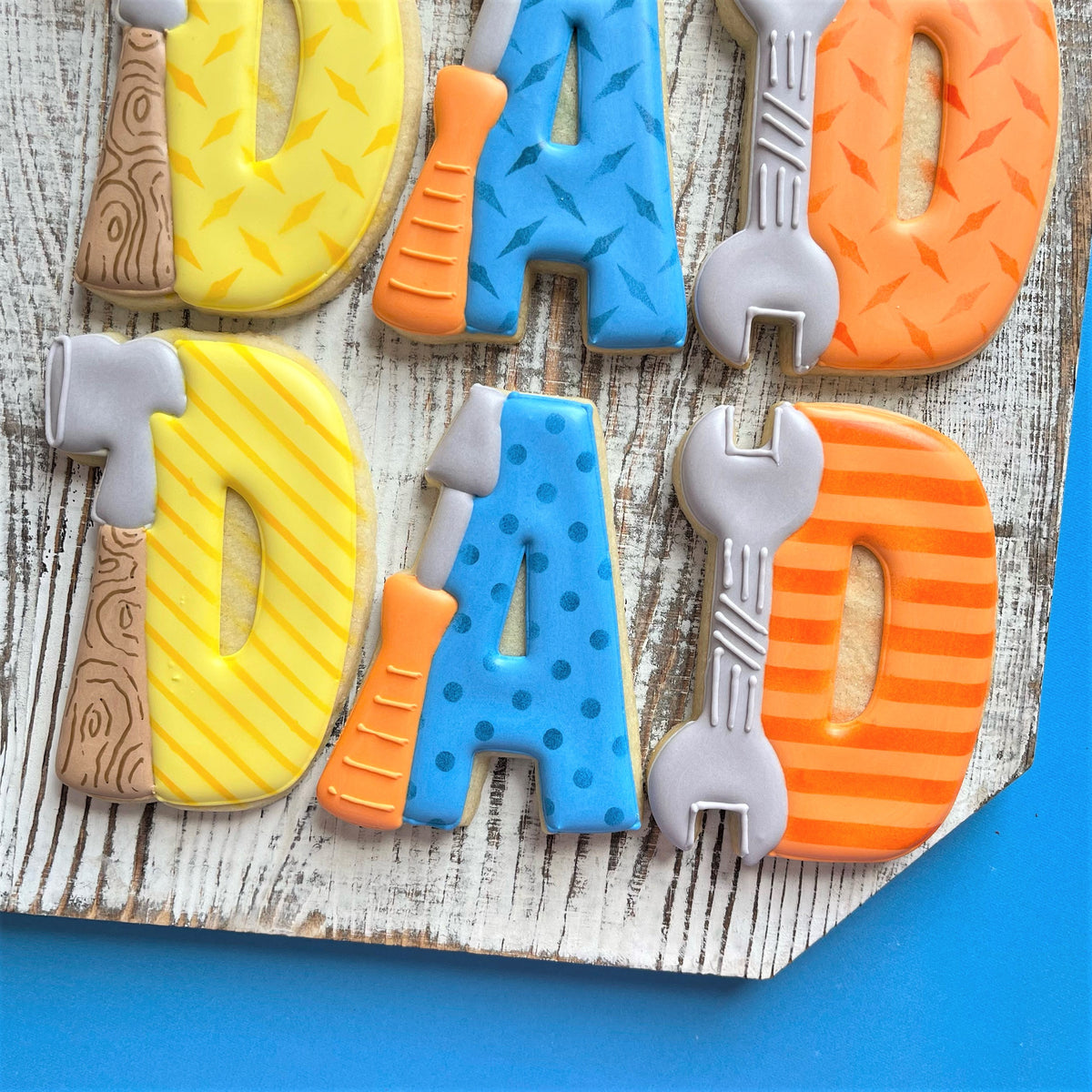 Vibrantly colored sugar cookies shaped like dad with tool-themed icing in yellow hammer blue wrench and orange screwdriver colors