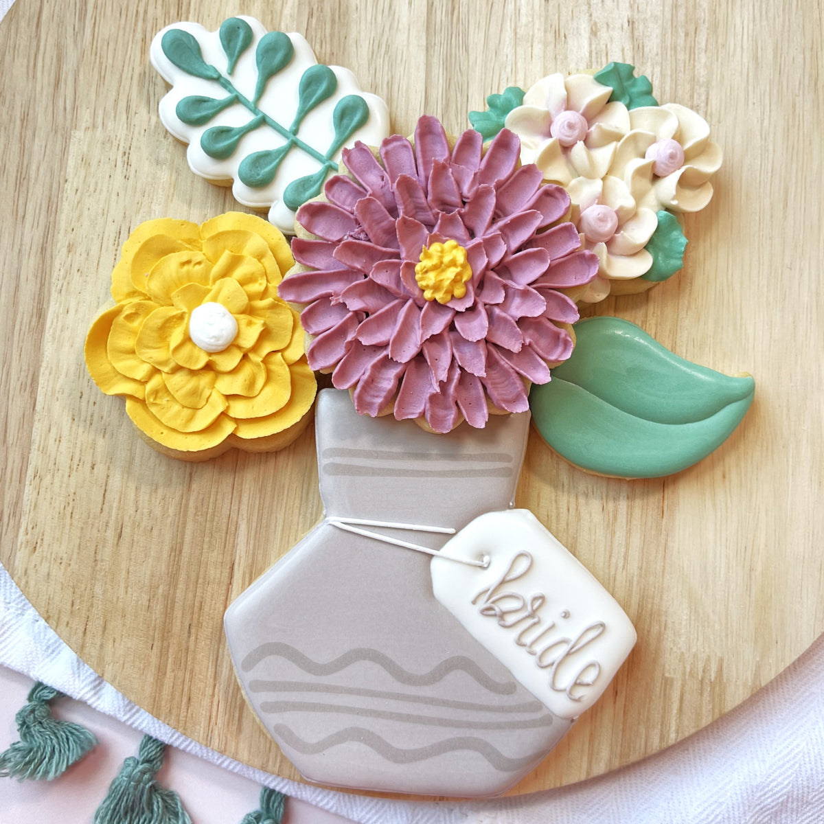 A light gray sugar cookie vase with wavy stripes holds yellow purple and beige floral cookies from flower vase 6pc set