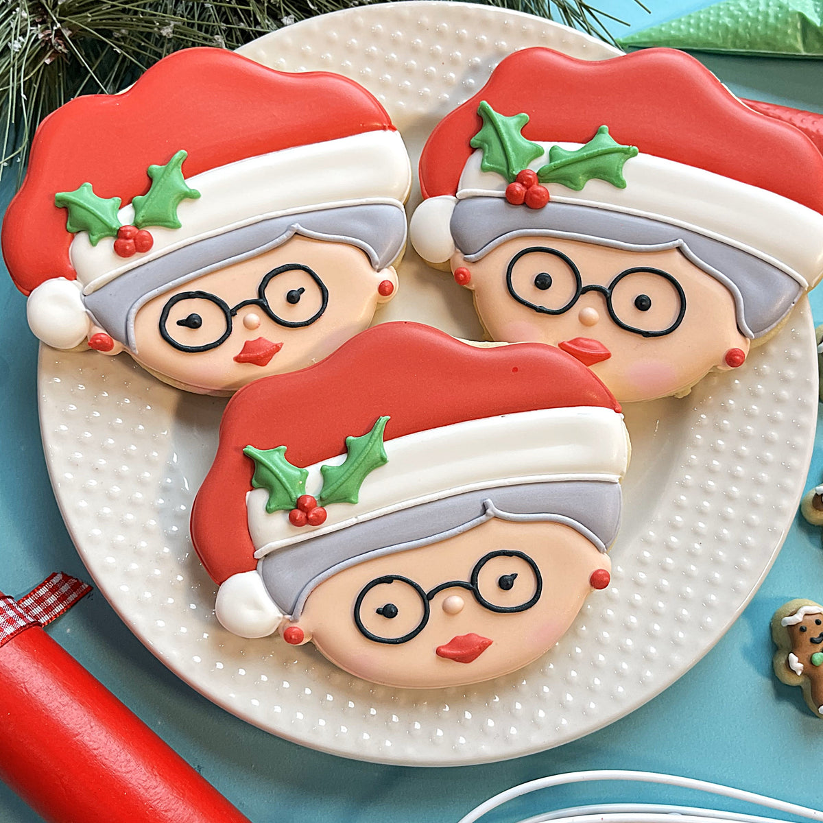 Three intricately decorated sugar cookies shaped like mrs claus wearing red santa hats with white trim using cookie cutter
