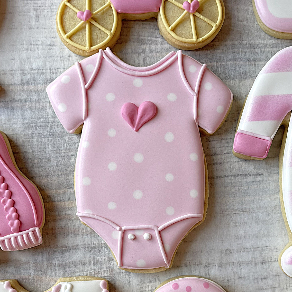Pink polka-dotted baby onesie cookie decorated with fondant heart made using baby onesie cookie cutter