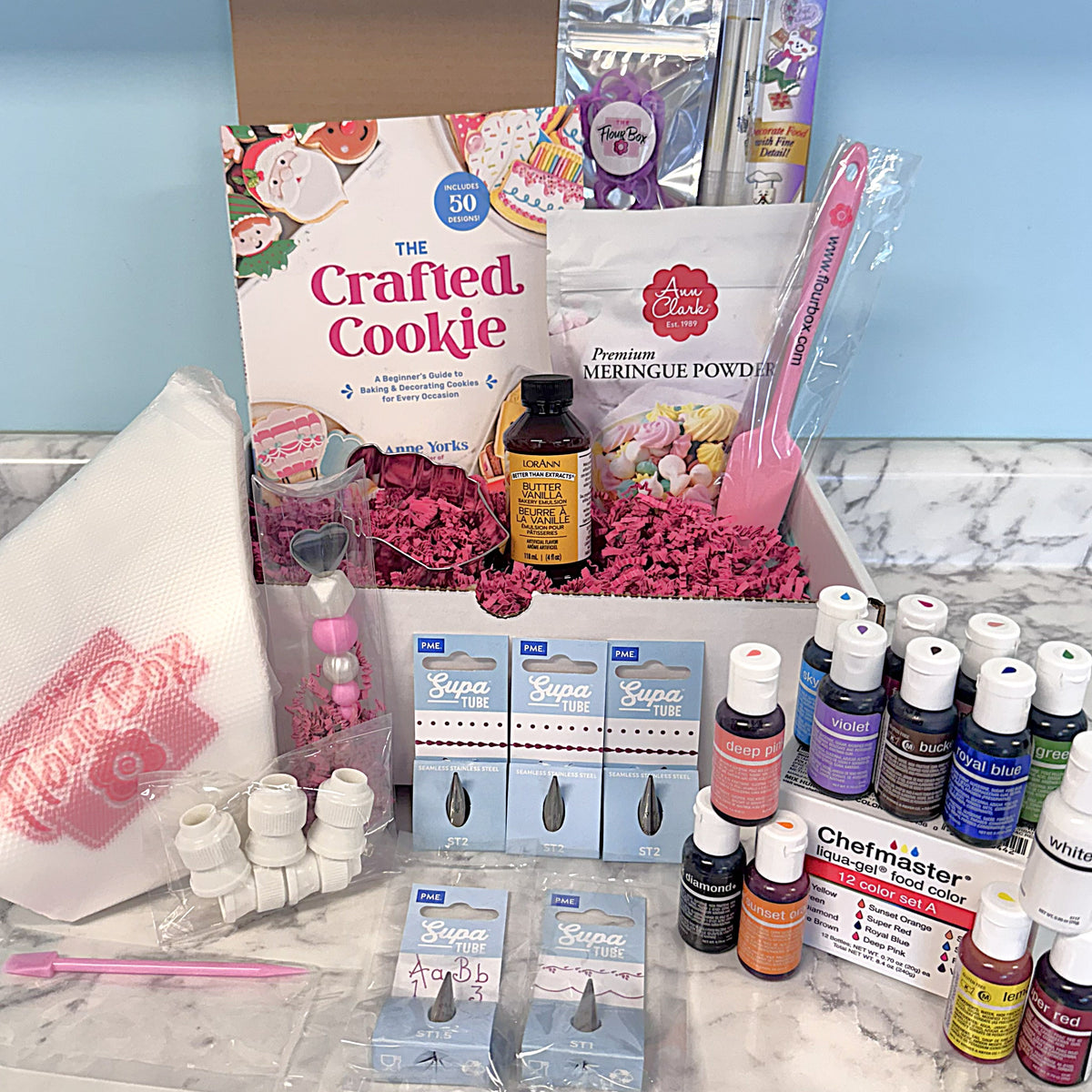 The cookie decorating starter kit box with a beginner’s guide and supplies like meringue powder and food coloring bottles