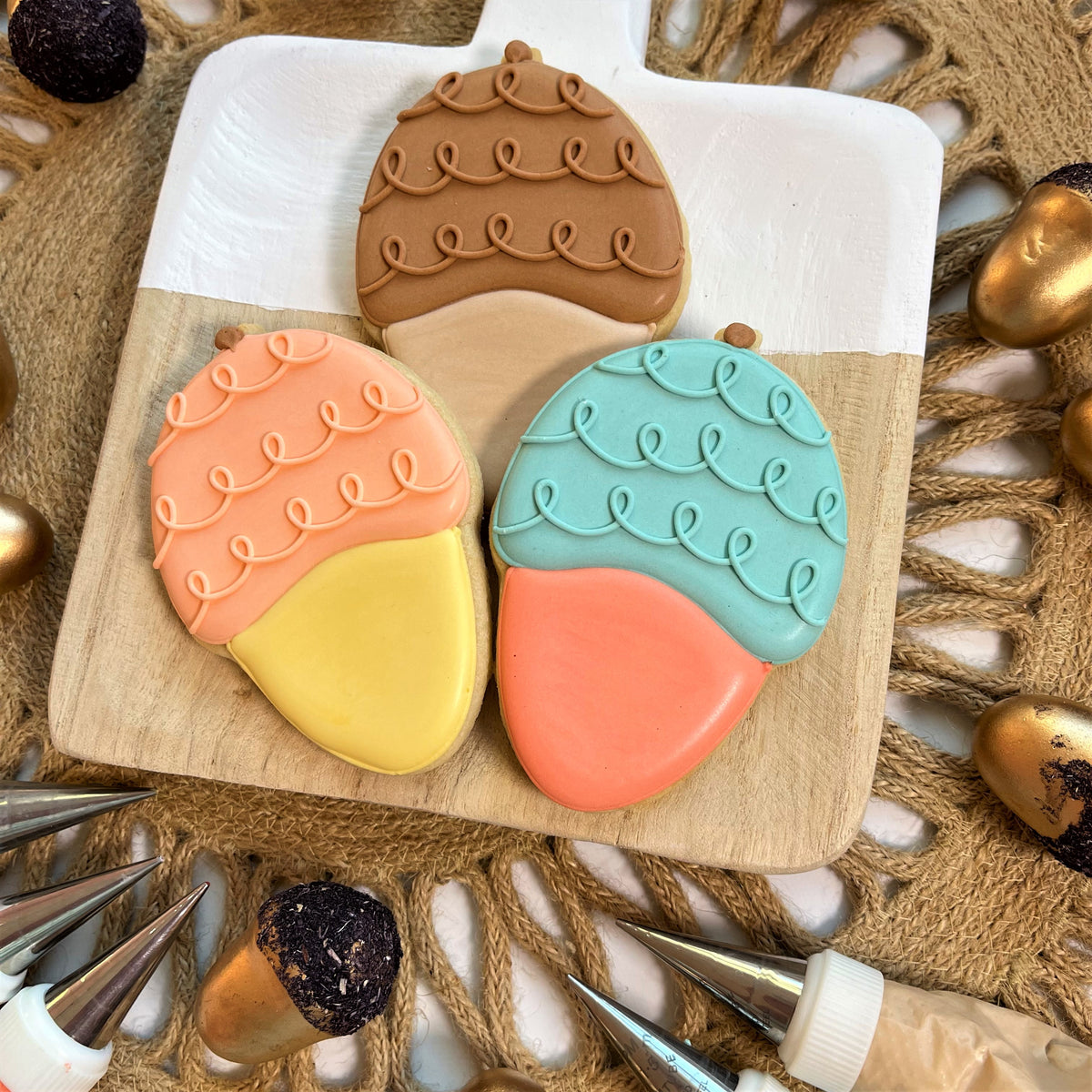 Three acorn doodle cookies with smooth fondant caps in brown peach teal and contrasting beige yellow coral bottoms