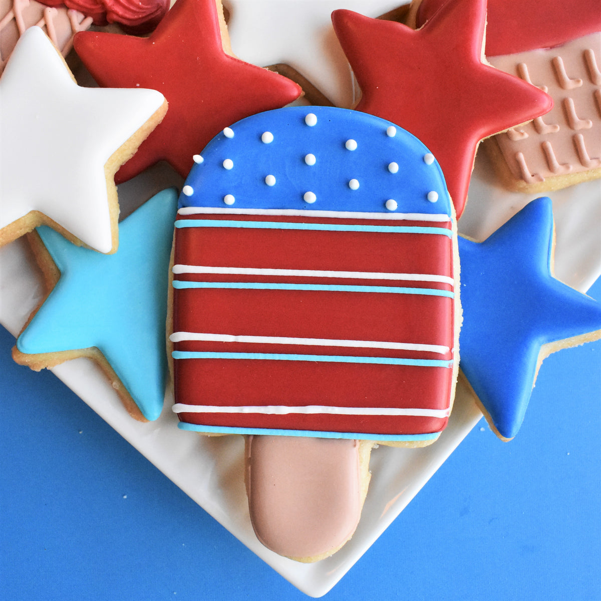 A patriotic red white and blue frosted cookie shaped like a popsicle with white dots and stripes for ice cream decorating class recording