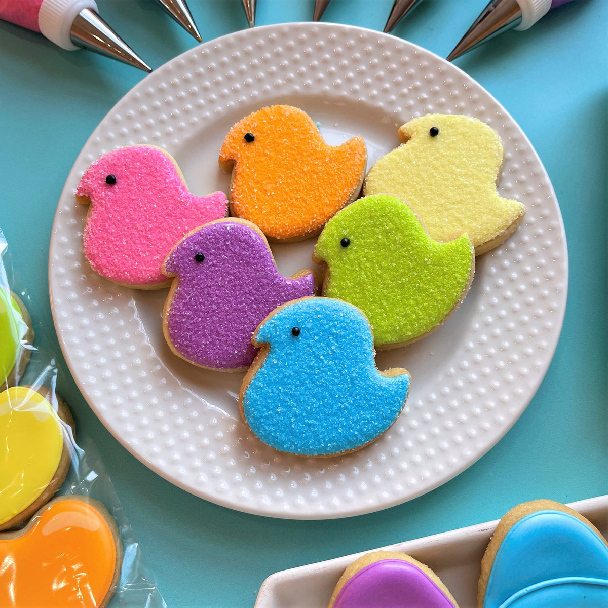 Colorful sugar-coated mini easter chick cookies in pink orange yellow purple and blue on a white plate