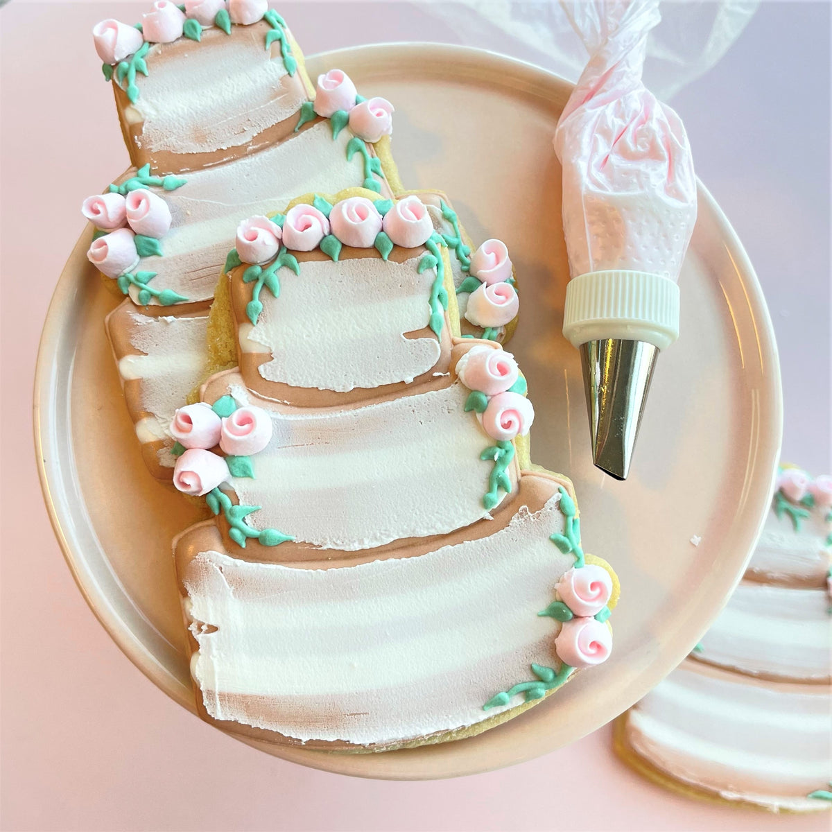 Rustic wedding cake cookie cutter shaping delicate multi-tiered cookies decorated with pink roses and mint-green vines