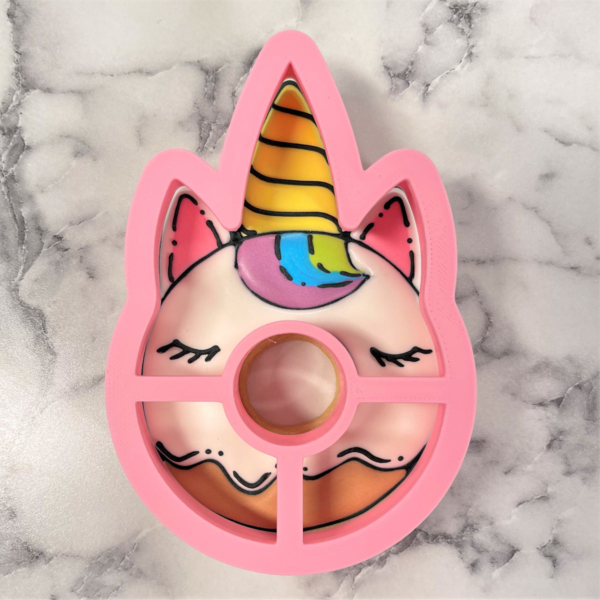 Unicorn donut cookie cutter in pink with a rainbow-striped horn and colorful facial features for baking fun