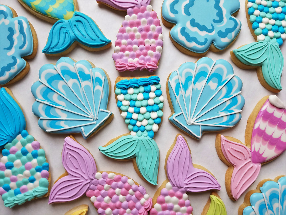 Pastel blue and pink mermaid tail-shaped cookies with intricate icing made using a mermaid tail cookie cutter